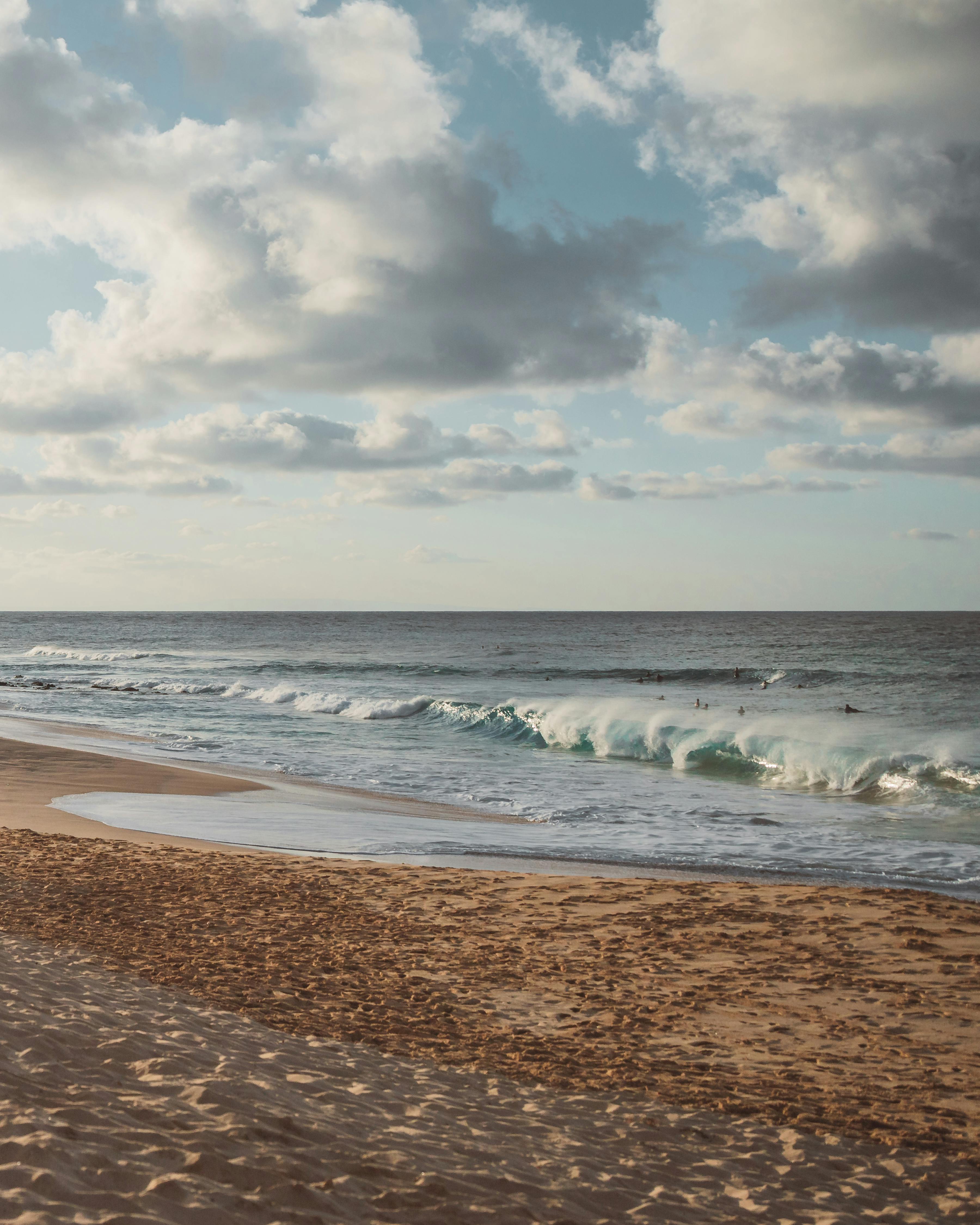 sea waves crashing on shore under white clouds