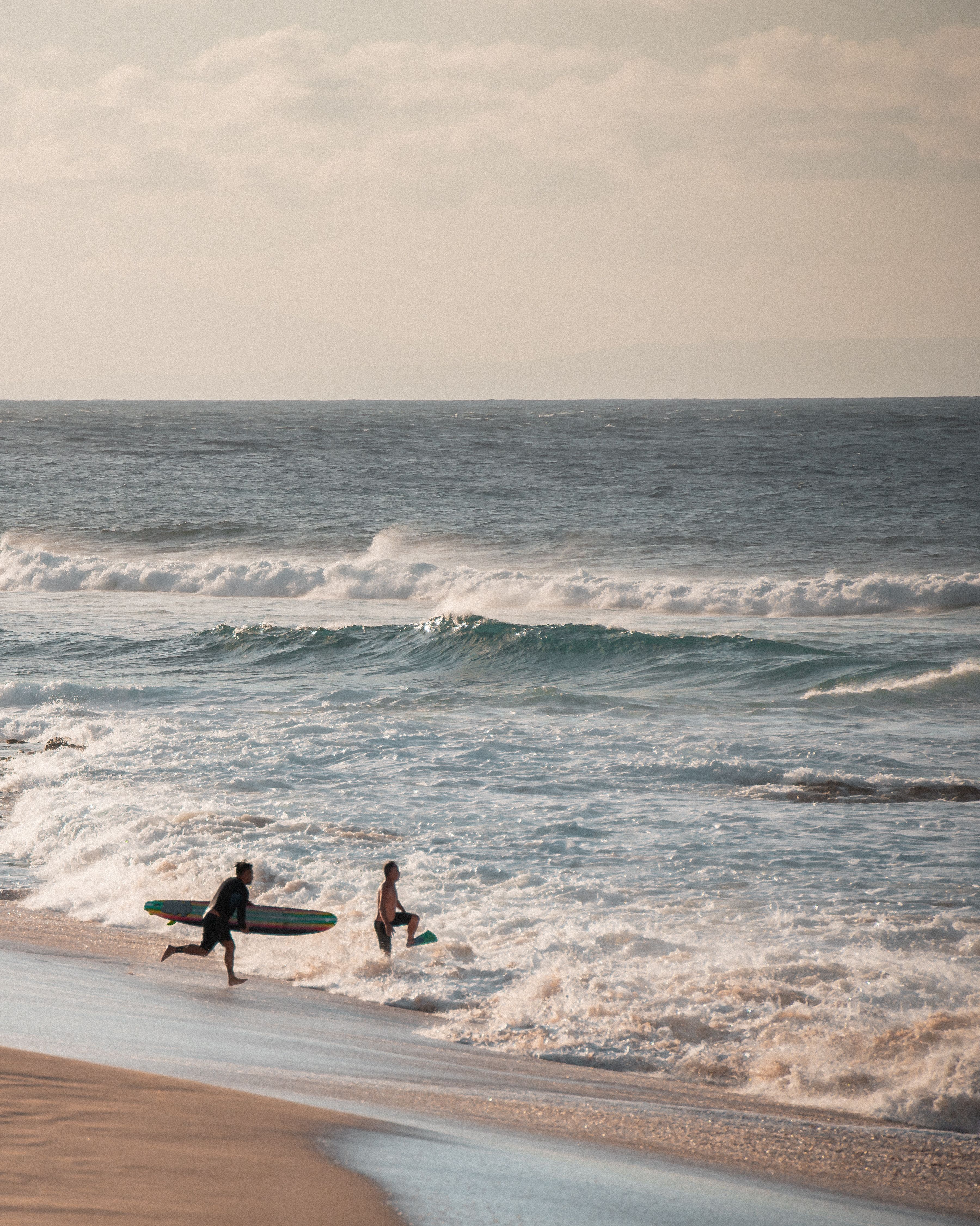 Two surfers running into the waves at sunset — photo by Jess Loiterton on Pexels