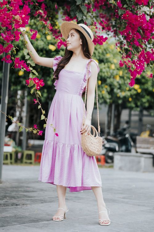Free Young trendy ethnic female in straw hat with handbag in trendy apparel touching blossoming flower on tree in town while looking away Stock Photo
