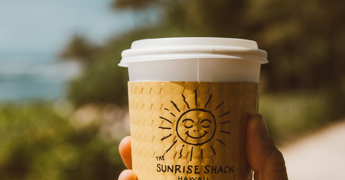 Photo by Jess Loiterton A hand holds a coffee cup from The Sunrise Shack, outdoors in a sunny Hawaiian setting.