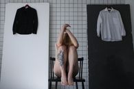 一名女子若有所思地坐在铺着瓷砖的极简主义房间里，椅子两侧放着衬衫