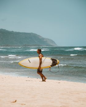 一名男子手持冲浪板，在海浪与海岸线的背景中，行走于沙滩上