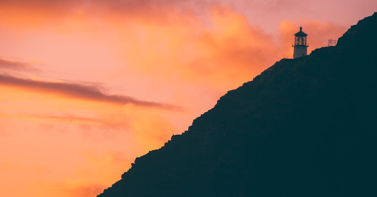 Photo by Jess Loiterton Silhouette of Makapu'u lighthouse against a vibrant sunset sky in Waimanalo Beach, Hawaii.