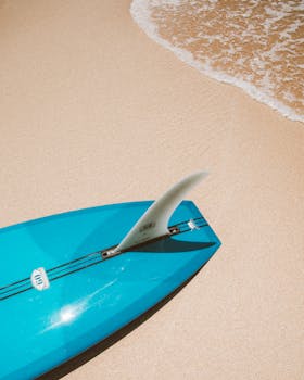Blue surfboard resting on a sandy beach in Hawaii, capturing a perfect beach day.
