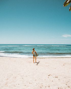 夏威夷海滩上，一个女人拿着冲浪板，在晴朗的蓝天下走向大海