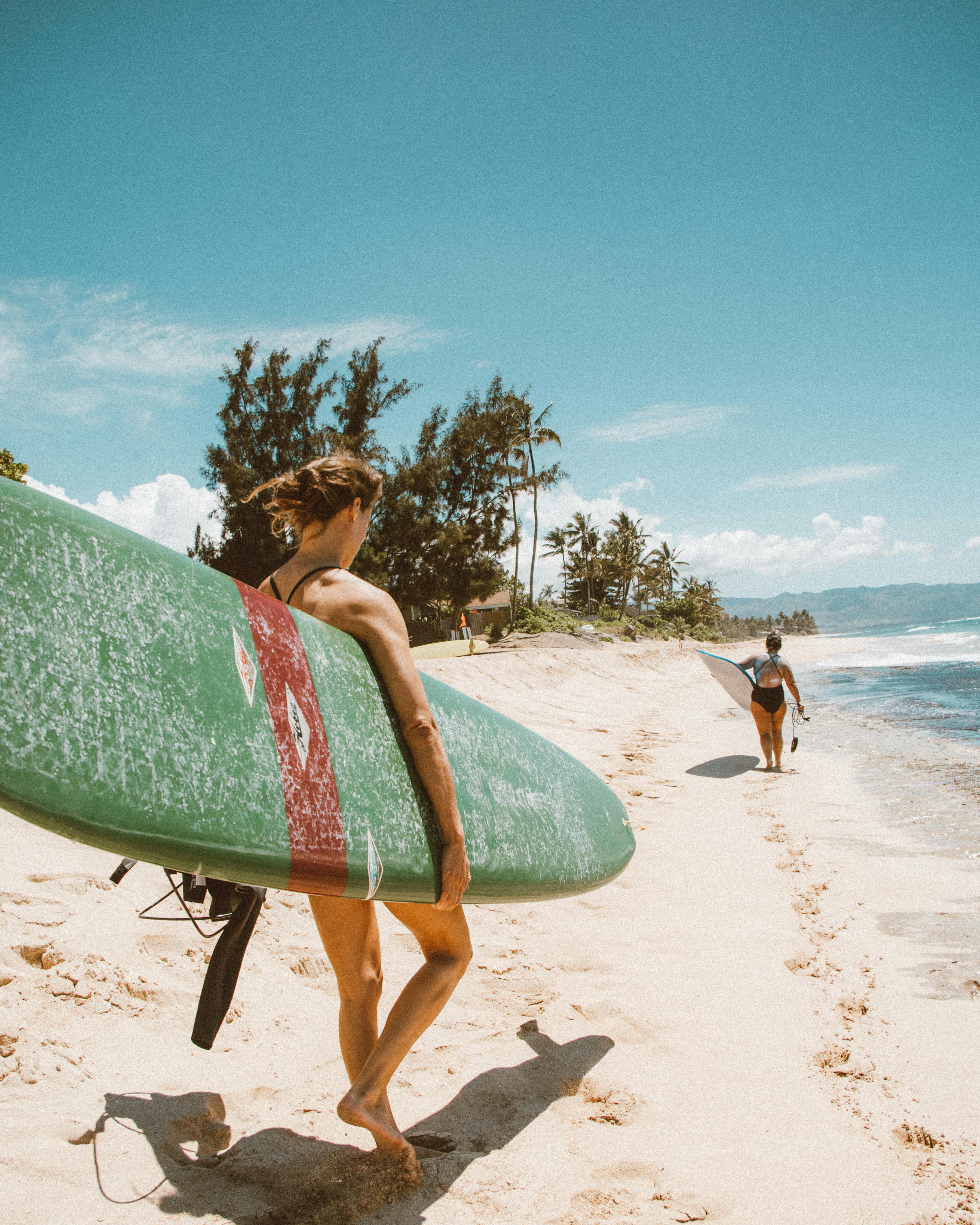 woman in black bikini holding blue surfboard on beach