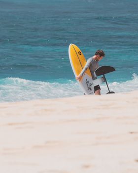 一名男子拿着箔纸板，站在夏威夷海浪汹涌的沙滩上