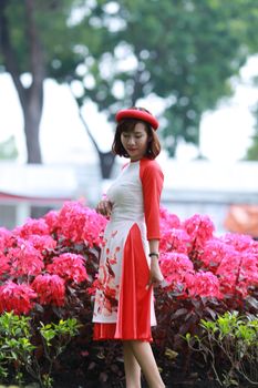 一位戴着红色贝雷帽的时尚女子，在充满活力的粉红色花丛中安详地摆着姿势