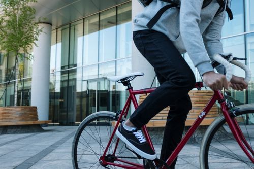 Free A cyclist in black jeans rides a red bike quickly through an urban area, showcasing fast urban transport. Stock Photo