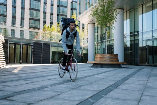 A cyclist with a backpack rides past modern architecture, epitomizing urban food delivery services.