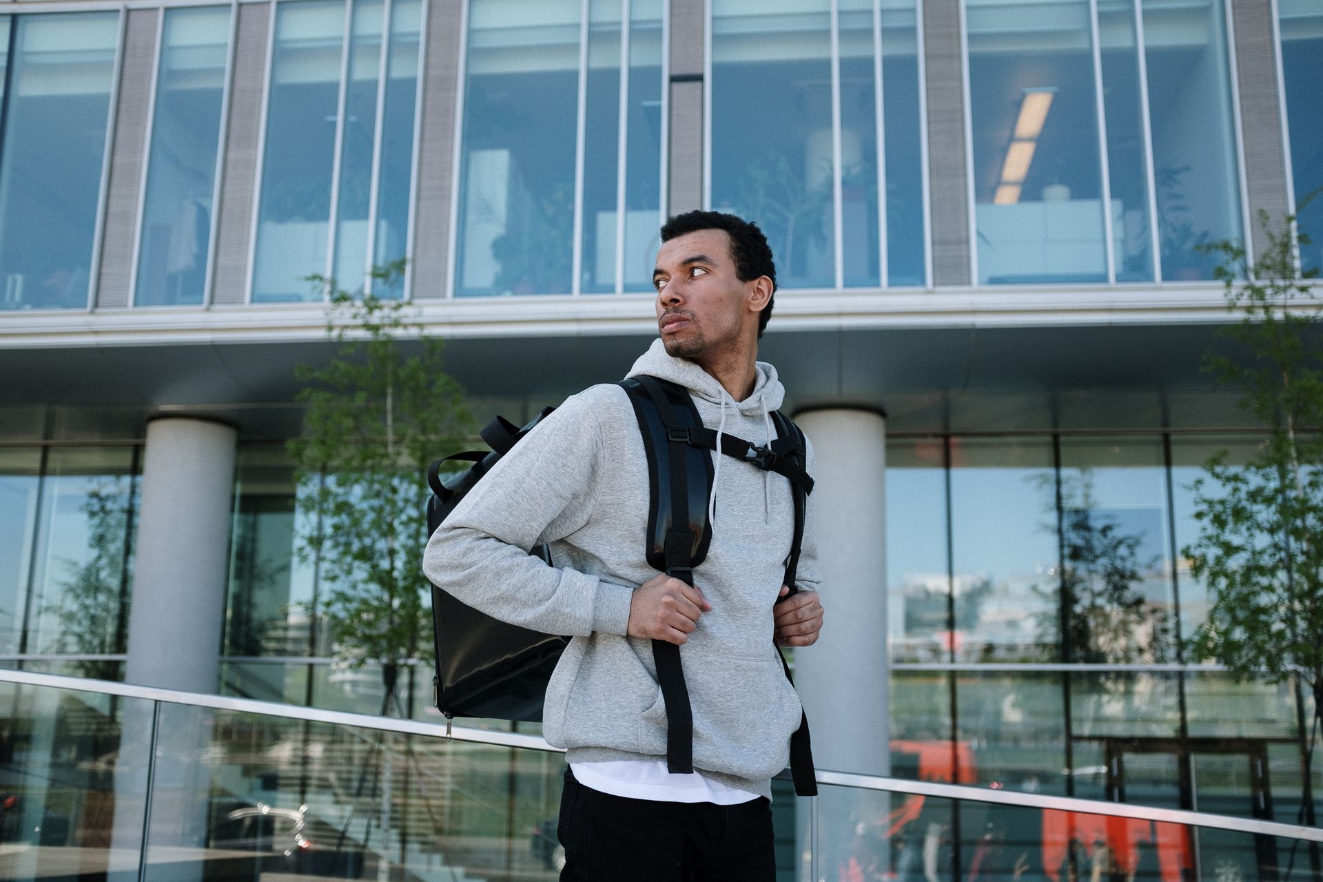 A man in casual attire with a backpack stands outside a modern office building.