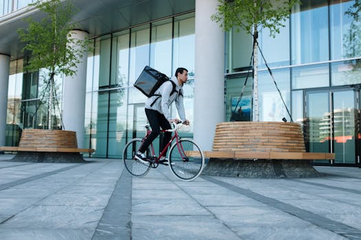 Bicycle courier delivering packages in an urban setting with modern architecture.