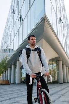 一名背着背包的骑车人站在城市里一栋建筑旁边