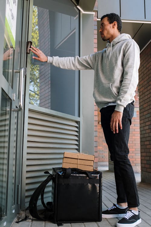 Man in Gray Sweater and Black Pants Standing Beside Glass Window