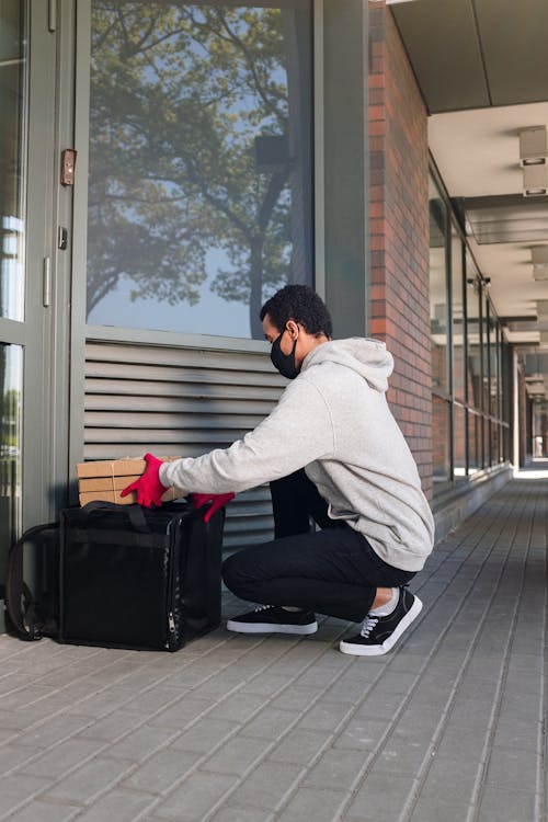 Man in Gray Hoodie and Black Pants Sitting on Black Luggage Bag