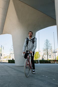 Young male cyclist delivering food in an urban setting under modern architecture.