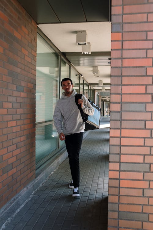 Man in Gray Jacket Standing Beside Brown Brick Wall