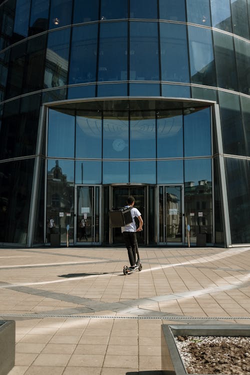 Man in White Shirt and Black Pants Riding on Black Skateboard in Front of Glass Building