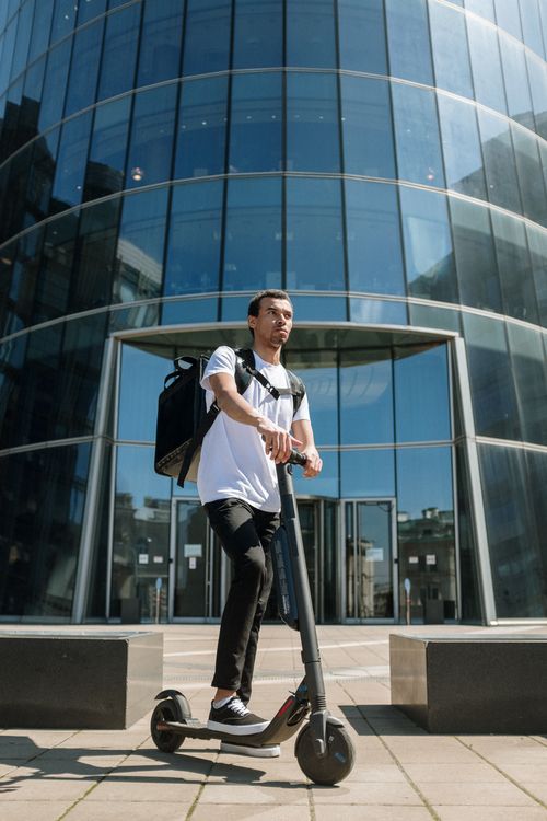 Free Man riding electric scooter for delivery in urban area outside office building. Stock Photo