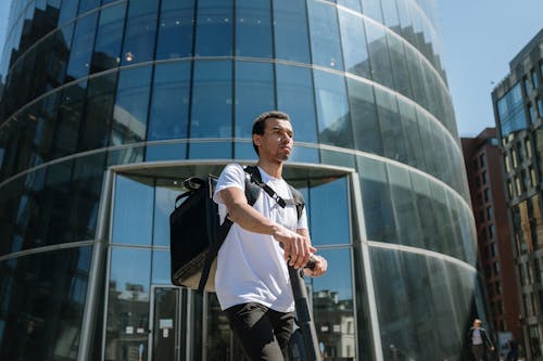 Man in White and Blue Polo Shirt and Black Pants Standing Near Glass Building