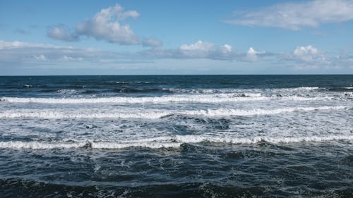 Picturesque view of foamy sea waves rolling towards coast beneath clear sky on sunny day