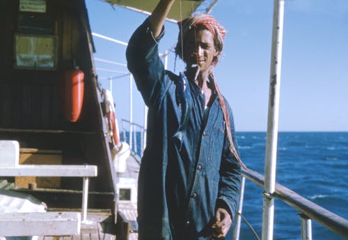 Man in Denim Coverall Standing on Boat with a Fish