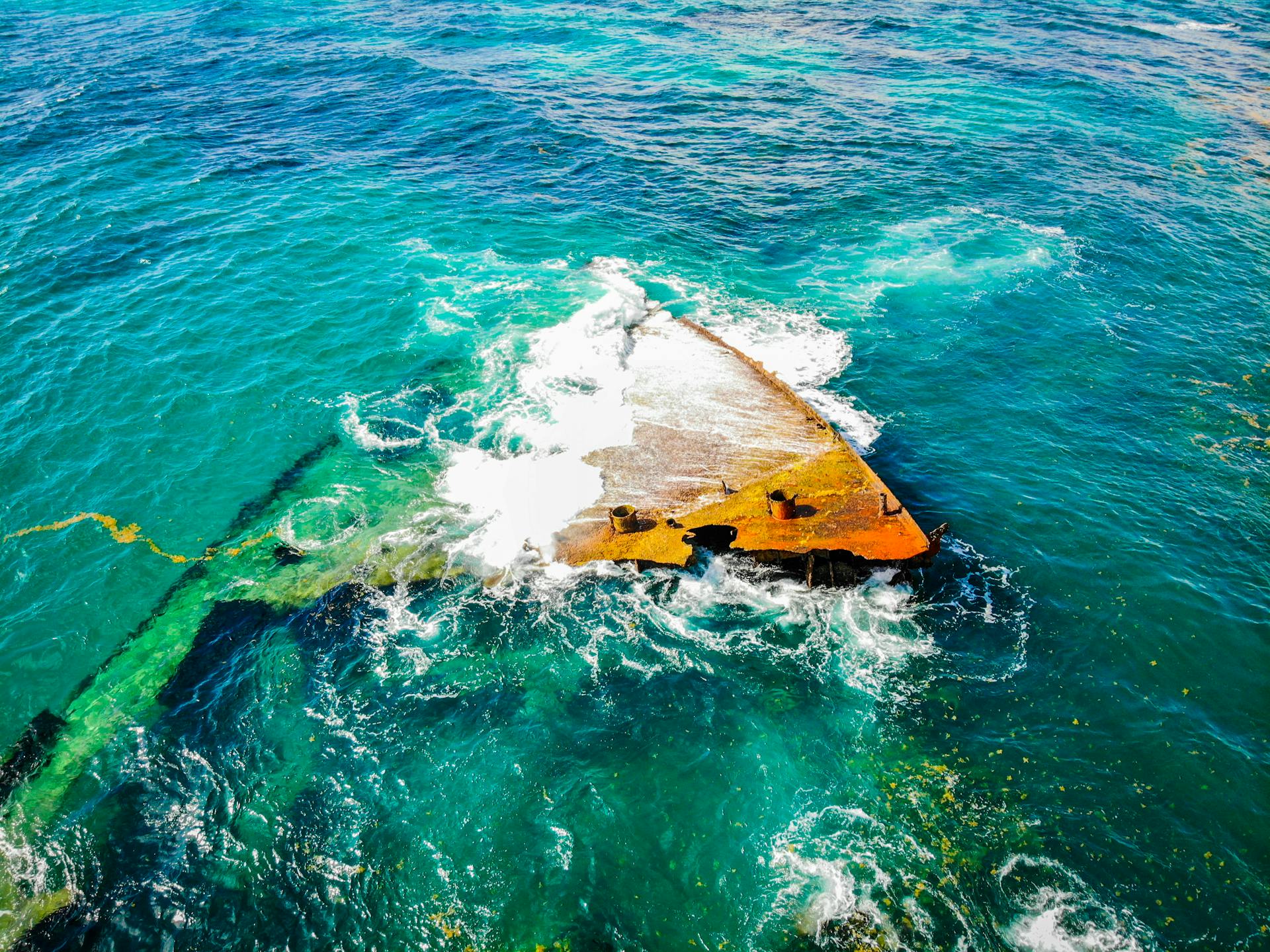 From above rusted grunge fragments of crashed boat lying in shallow sea and washed by clean green water