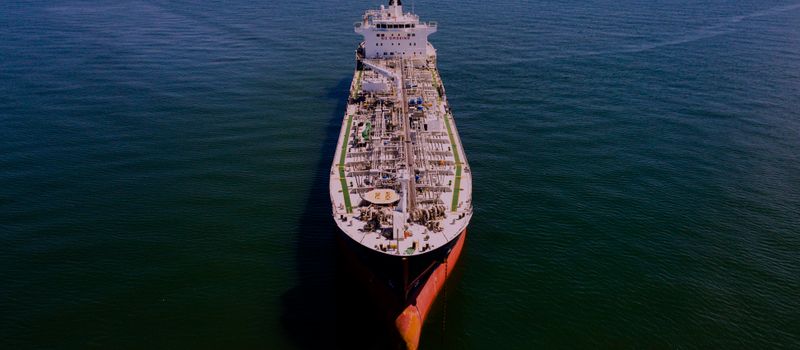 夕暮れの海を進むタンカー。ホルムズ海峡の緊張緩和で原油相場が落ち着く様子を表すイメージ。