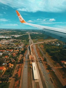 A scenic aerial view of Brasília with cityscape and highways beneath the plane wing, showcasing vibrant landscapes.