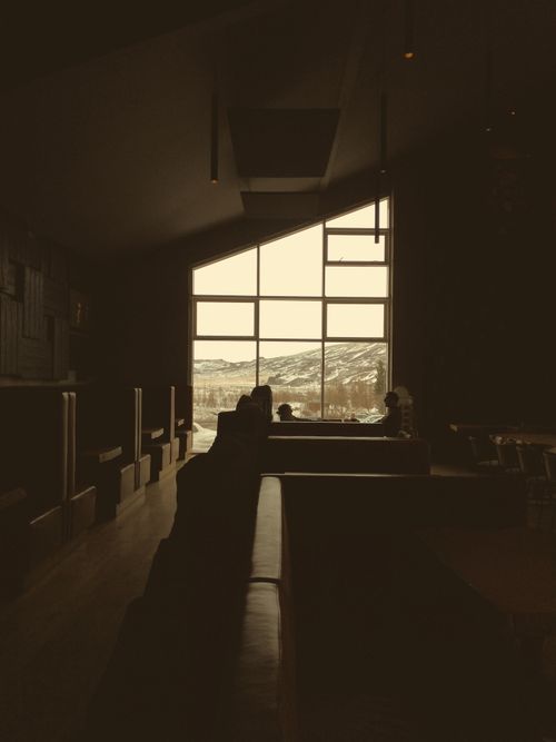 Free Dark brown tables and couches under angled ceiling in empty dark cafe with mountain through big window Stock Photo