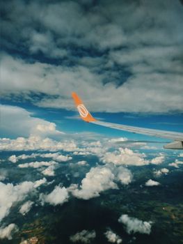 View from plane turbine of modern white wing and cloudy blue sky over breathtaking green natural landscape