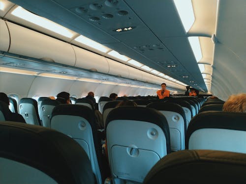 Inside of modern airplane cabin with passengers sitting on comfortable seats and cabin crew standing at passageway