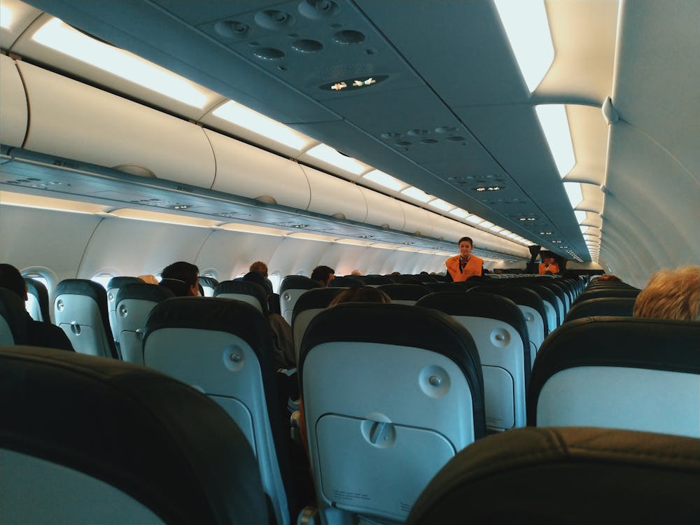 Free Inside of modern airplane cabin with passengers sitting on comfortable seats and cabin crew standing at passageway Stock Photo