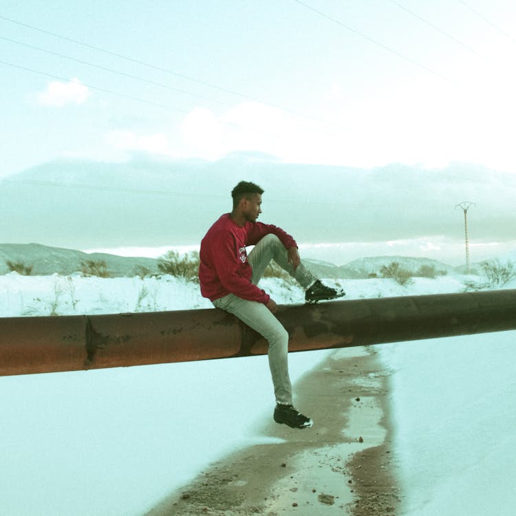 African American Hipster Sitting At Pipeline In Snowy Field