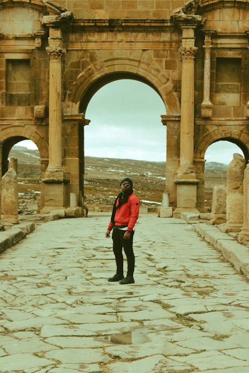Unrecognizable ethnic traveler standing near old stone yellow arch