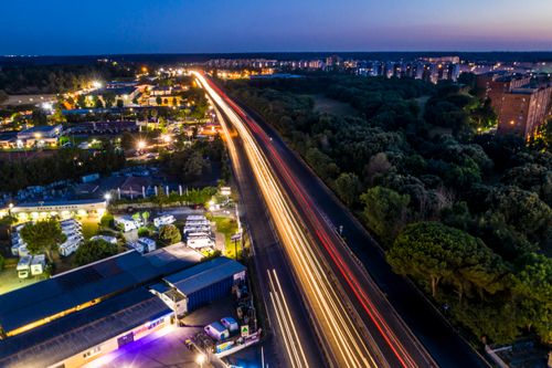 Free Drone view of modern illuminated road located among green trees and industrial buildings at dusk Stock Photo