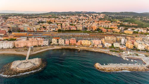 Aerial view of turquoise wavy bay and long seafront with boats surrounded by small colorful houses