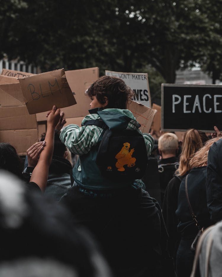 People Protesting On The Street With  A Child Sitting On A Man's Shoulder 