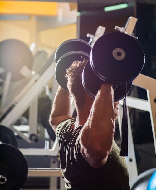 Strong faceless sportsman lifting dumbbell in gym
