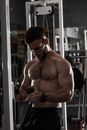 Brutal shirtless sportsman standing with cable rope triceps extension in hands during training in modern equipped gym