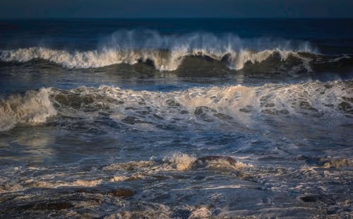 Severe view of powerful waves of foamy blue sea rolling near shore in evening
