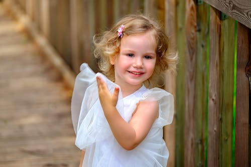 Happy little girl in white dress on wooden terrace