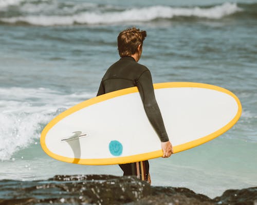 Woman in Black Tank Top Holding White Surfboard Standing on Beach