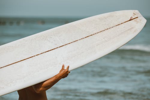 Person Holding White Surfboard Near Body of Water