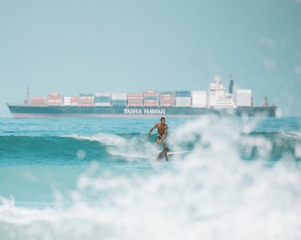 Surfer catching waves in Honolulu with a cargo ship in background, showcasing adventure and travel.