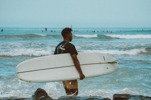 Man in Black and Red Shirt Holding White Surfboard on Beach