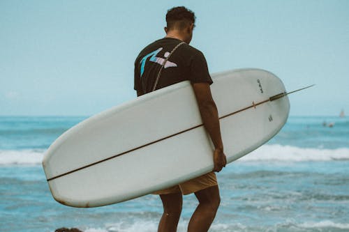 Man in Blue and White Shirt Holding White Surfboard