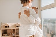 两个年幼的孩子在一个明亮舒适的房间里，亲切地拥抱在一起，旁边还有一个玩具屋