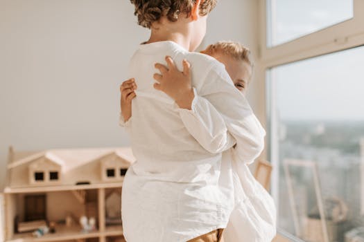 两个年幼的孩子在一个明亮舒适的房间里，亲切地拥抱在一起，旁边还有一个玩具屋