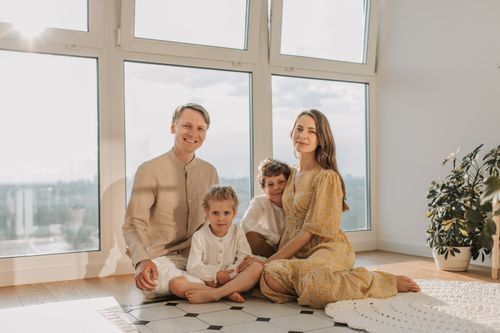 Free A cheerful family of four sitting together on the floor of a sunlit living room. Stock Photo